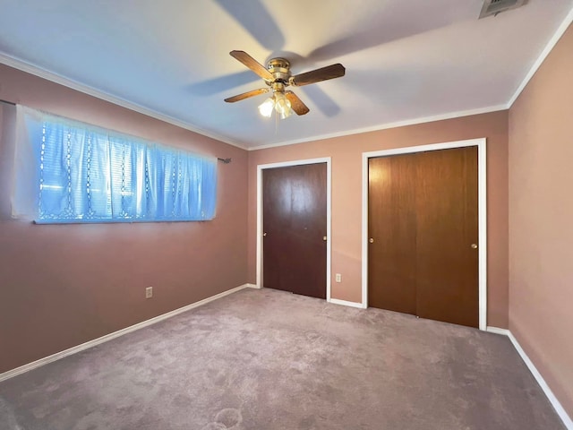 unfurnished bedroom featuring crown molding, two closets, visible vents, carpet flooring, and baseboards