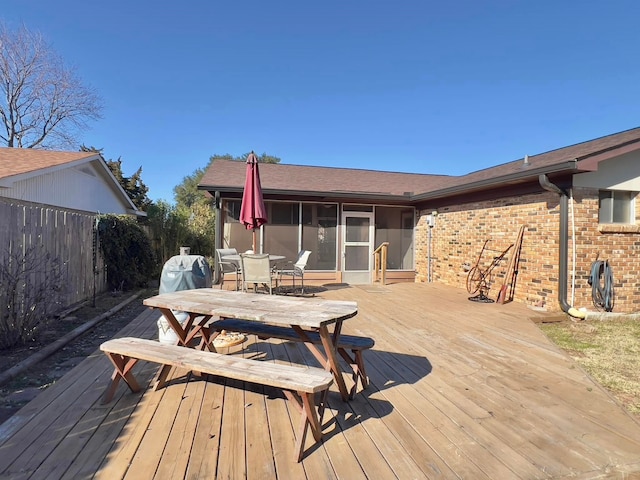 wooden deck featuring outdoor dining area, fence, and a sunroom