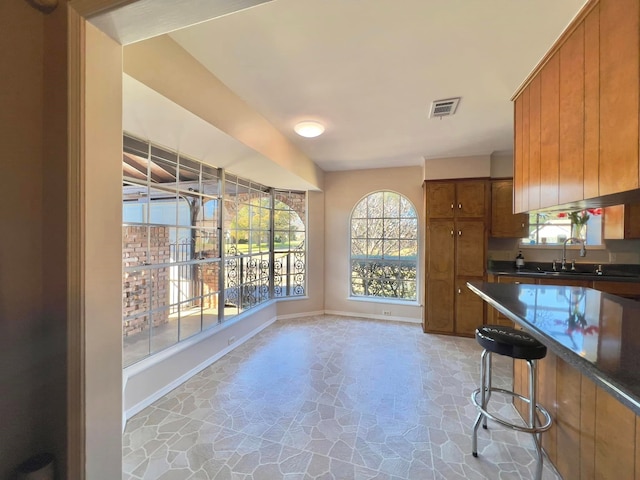 kitchen with brown cabinets, dark countertops, visible vents, stone finish floor, and baseboards