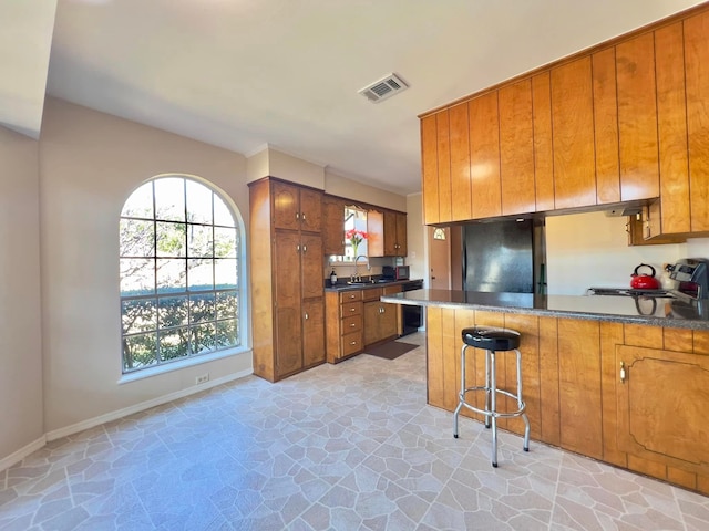 kitchen with brown cabinetry, black fridge, a sink, and visible vents