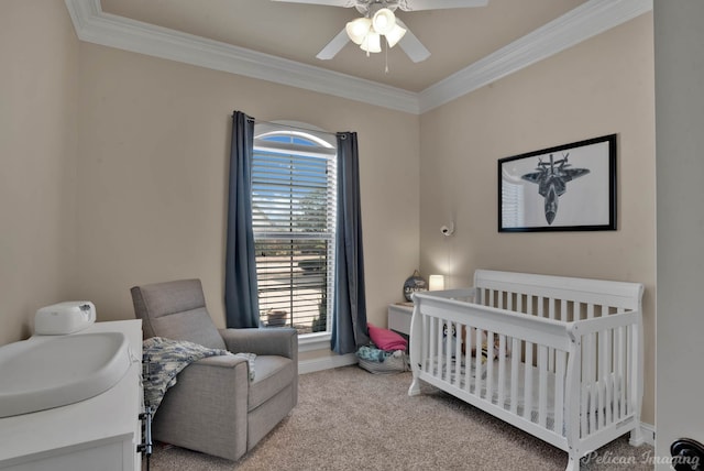 carpeted bedroom with a ceiling fan, crown molding, a crib, and baseboards