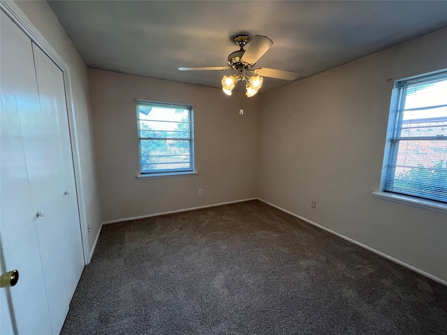 unfurnished bedroom featuring dark colored carpet, a closet, and ceiling fan