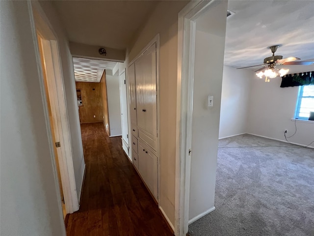 hallway featuring dark colored carpet, dark wood-style flooring, and baseboards