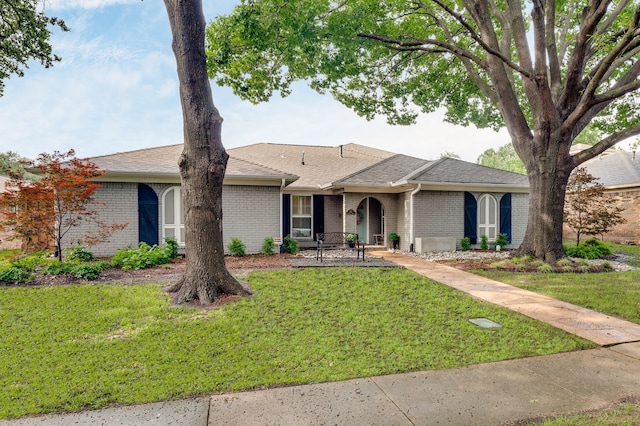 ranch-style home featuring a shingled roof, brick siding, and a front lawn