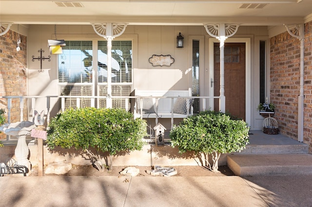 view of exterior entry featuring covered porch, visible vents, and brick siding