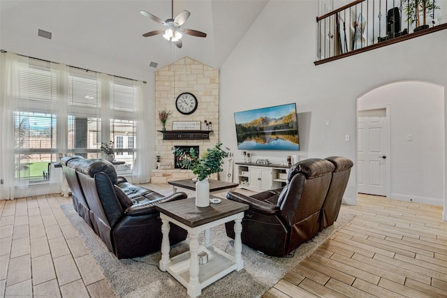 living room featuring wood finish floors, arched walkways, a fireplace, visible vents, and high vaulted ceiling