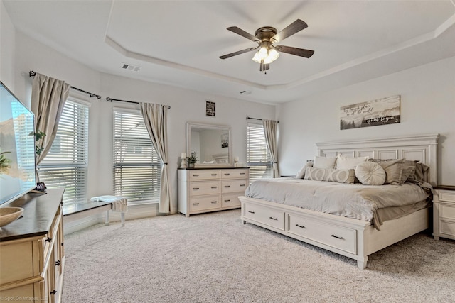 bedroom with light carpet, ceiling fan, visible vents, and a raised ceiling