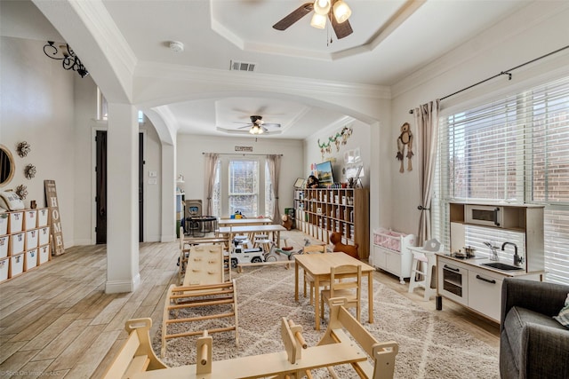 living area featuring a ceiling fan, light wood-style floors, arched walkways, a raised ceiling, and visible vents