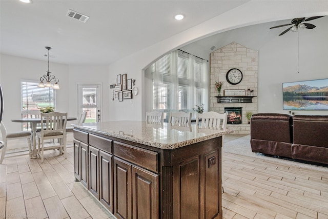 kitchen featuring light stone counters, visible vents, decorative light fixtures, a fireplace, and ceiling fan with notable chandelier