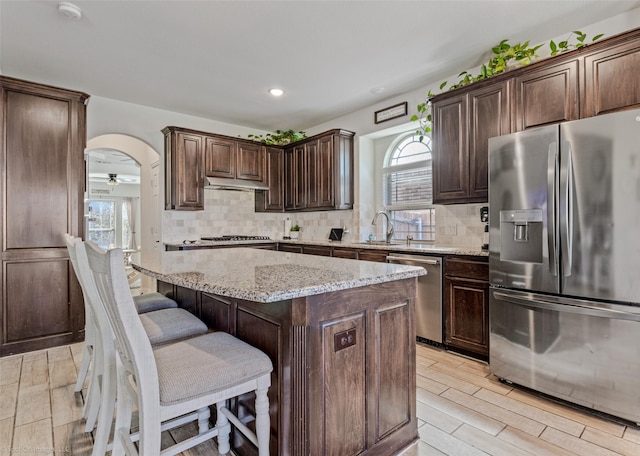 kitchen featuring stainless steel appliances, arched walkways, a sink, and dark brown cabinetry