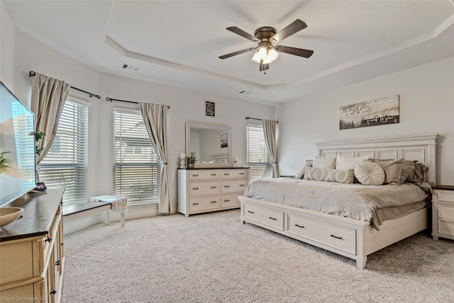 bedroom with a tray ceiling, ceiling fan, visible vents, and light carpet