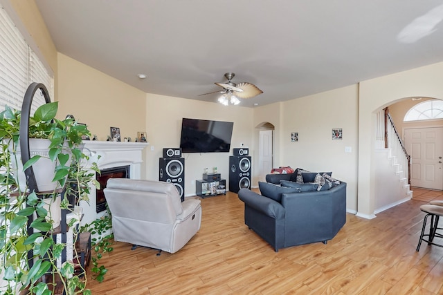 living area with light wood-style flooring, a fireplace, arched walkways, and a wealth of natural light