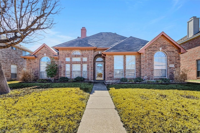 view of front of house featuring brick siding, a front lawn, and a chimney