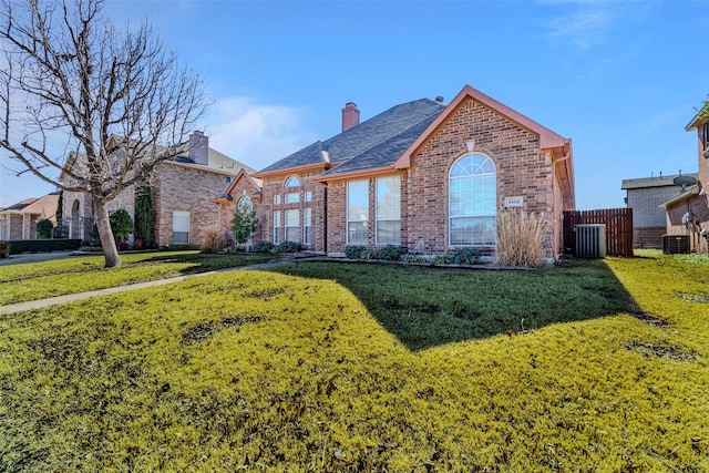 view of front of home with central AC unit, brick siding, a chimney, and a front yard