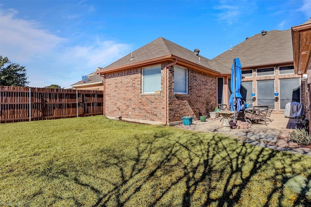 back of house with roof with shingles, brick siding, a patio, a lawn, and fence