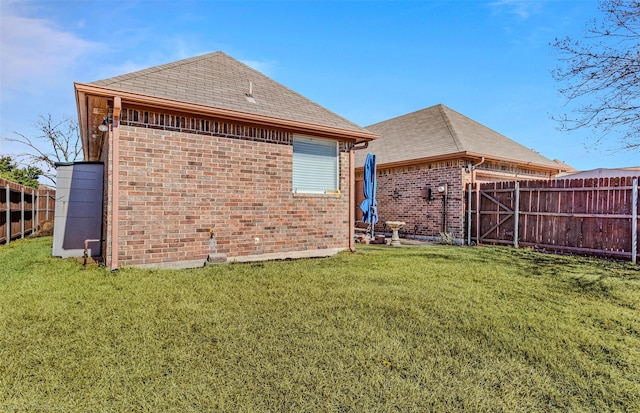 rear view of house with fence private yard, brick siding, roof with shingles, and a yard