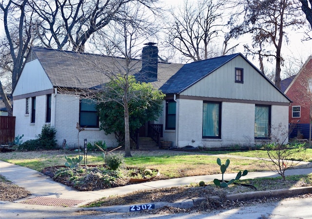 view of front of house featuring roof with shingles, brick siding, a chimney, and a front yard