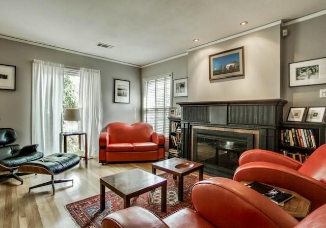 living area with visible vents, wood finished floors, a wealth of natural light, and a glass covered fireplace