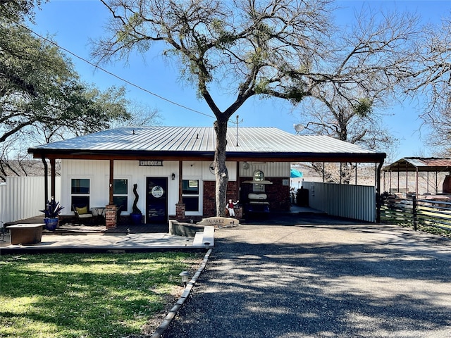 bungalow-style home with gravel driveway, metal roof, fence, a carport, and a front lawn