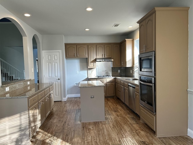 kitchen with appliances with stainless steel finishes, light stone counters, dark wood-style flooring, a center island, and under cabinet range hood