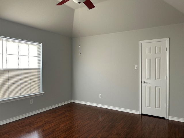 empty room featuring dark wood-style floors, vaulted ceiling, baseboards, and a ceiling fan