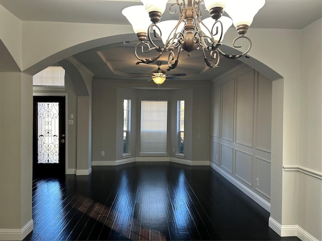 foyer with arched walkways, visible vents, baseboards, dark wood-style floors, and a tray ceiling