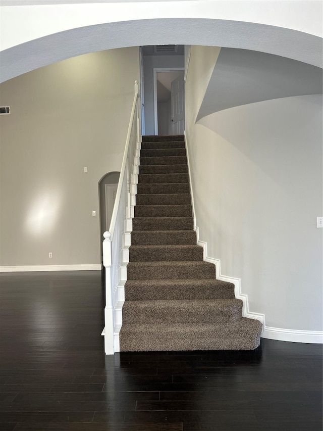 staircase with arched walkways, wood finished floors, visible vents, and baseboards