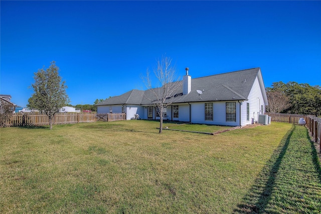 rear view of property with a yard, a chimney, a fenced backyard, and central air condition unit