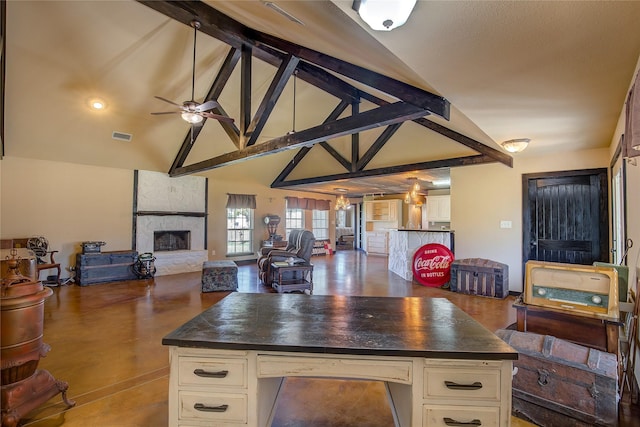 kitchen featuring a ceiling fan, dark countertops, beam ceiling, and a stone fireplace