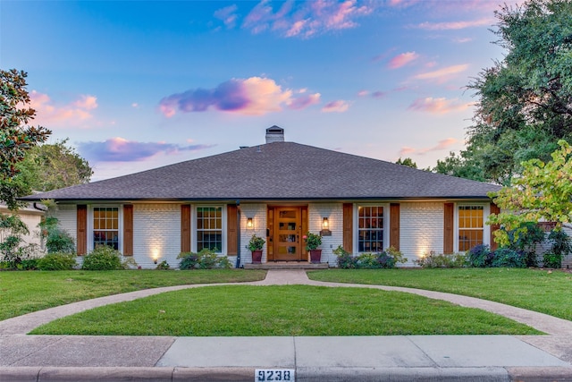 ranch-style home featuring a front lawn, a chimney, brick siding, and a shingled roof