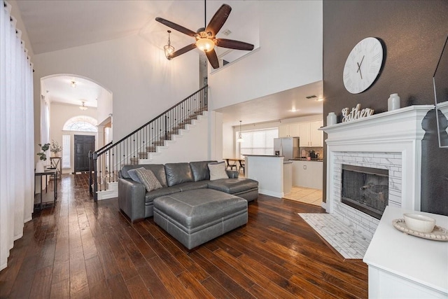 living room featuring a fireplace with flush hearth, arched walkways, dark wood-style flooring, and stairway