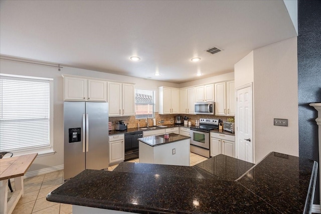 kitchen with light tile patterned floors, stainless steel appliances, visible vents, backsplash, and a center island