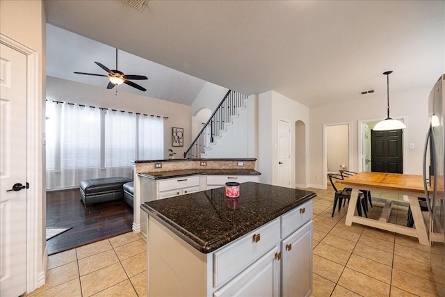 kitchen with light tile patterned floors, visible vents, arched walkways, a center island, and white cabinetry