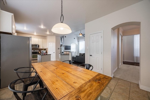 dining space with arched walkways, ceiling fan, light tile patterned floors, and baseboards