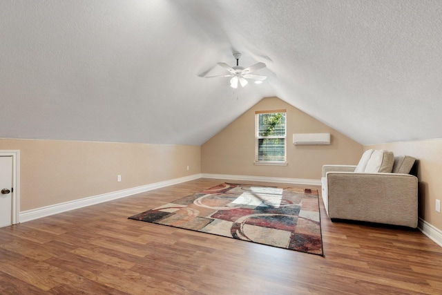 bonus room with a textured ceiling, vaulted ceiling, wood finished floors, and a wall mounted AC