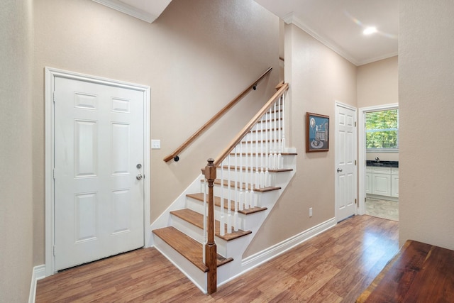 foyer entrance with baseboards, light wood finished floors, stairs, and crown molding