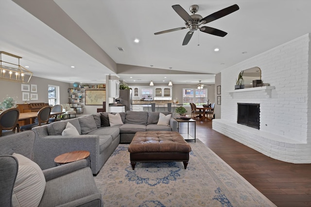 living room with recessed lighting, visible vents, dark wood-style floors, a brick fireplace, and ceiling fan with notable chandelier