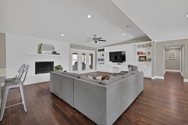 living area with lofted ceiling, built in shelves, dark wood-style flooring, and a brick fireplace