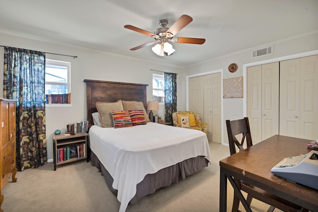 bedroom with visible vents, ornamental molding, multiple closets, and light colored carpet