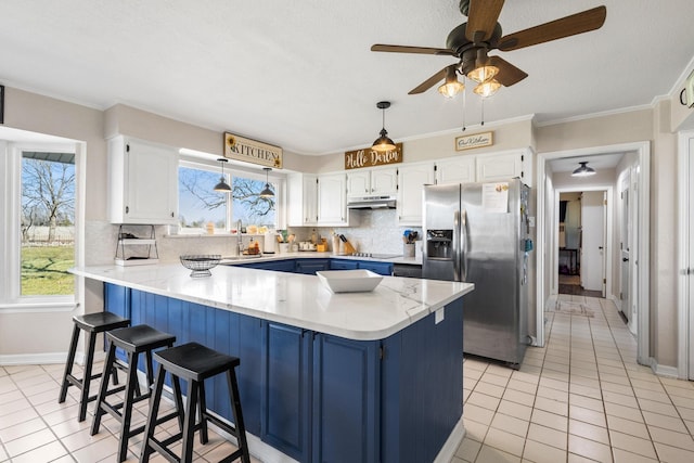 kitchen with stainless steel fridge, under cabinet range hood, blue cabinetry, white cabinetry, and a sink