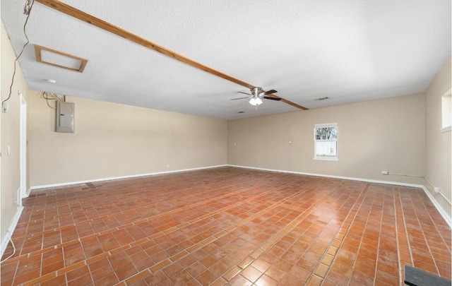 spare room with attic access, electric panel, baseboards, a ceiling fan, and a textured ceiling