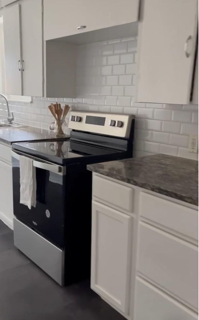 kitchen with dark countertops, stainless steel electric stove, white cabinets, and backsplash