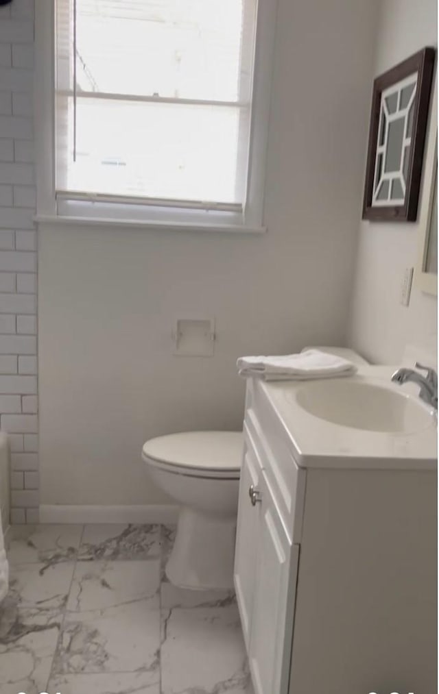 bathroom with toilet, marble finish floor, plenty of natural light, and vanity