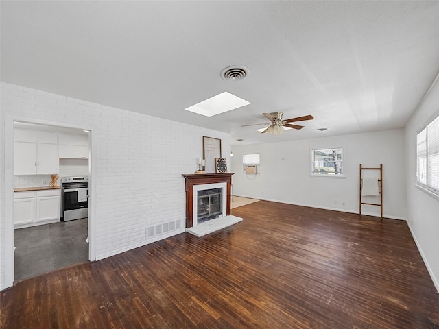 unfurnished living room featuring a fireplace with raised hearth, brick wall, dark wood-style floors, and visible vents