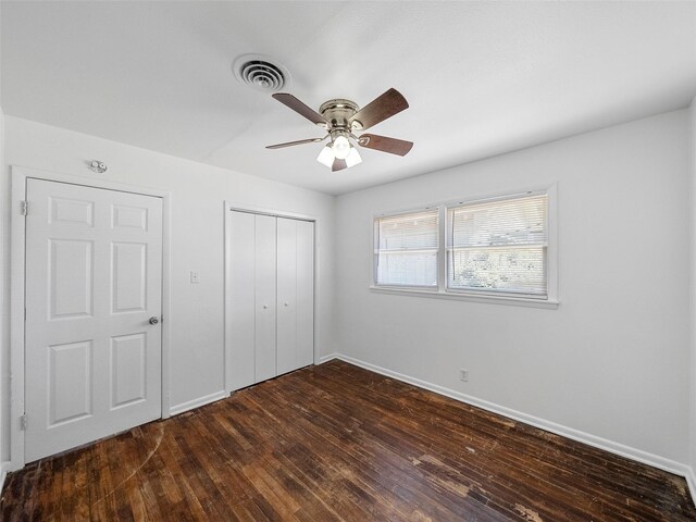 unfurnished bedroom featuring baseboards, visible vents, a ceiling fan, dark wood finished floors, and a closet