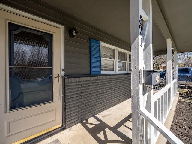 doorway to property featuring covered porch and brick siding