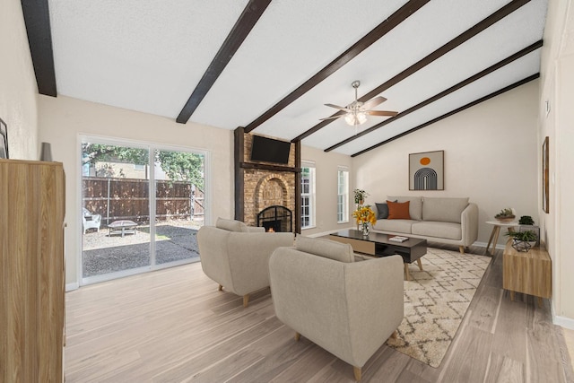 living area with beamed ceiling, light wood-style flooring, a textured ceiling, baseboards, and a brick fireplace