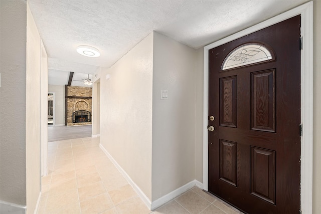 entryway with light tile patterned floors, baseboards, a textured ceiling, and a brick fireplace