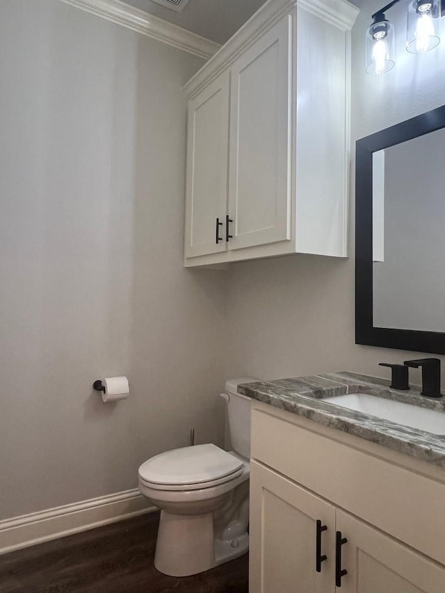 bathroom with baseboards, toilet, ornamental molding, wood finished floors, and vanity