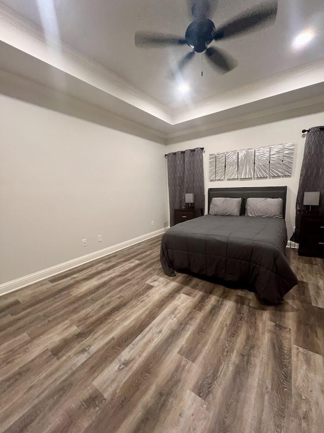 bedroom featuring a ceiling fan, a raised ceiling, baseboards, and wood finished floors